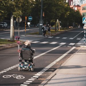 Une femme âgée utilise un fauteuil roulant électrique dans une piste cyclable.