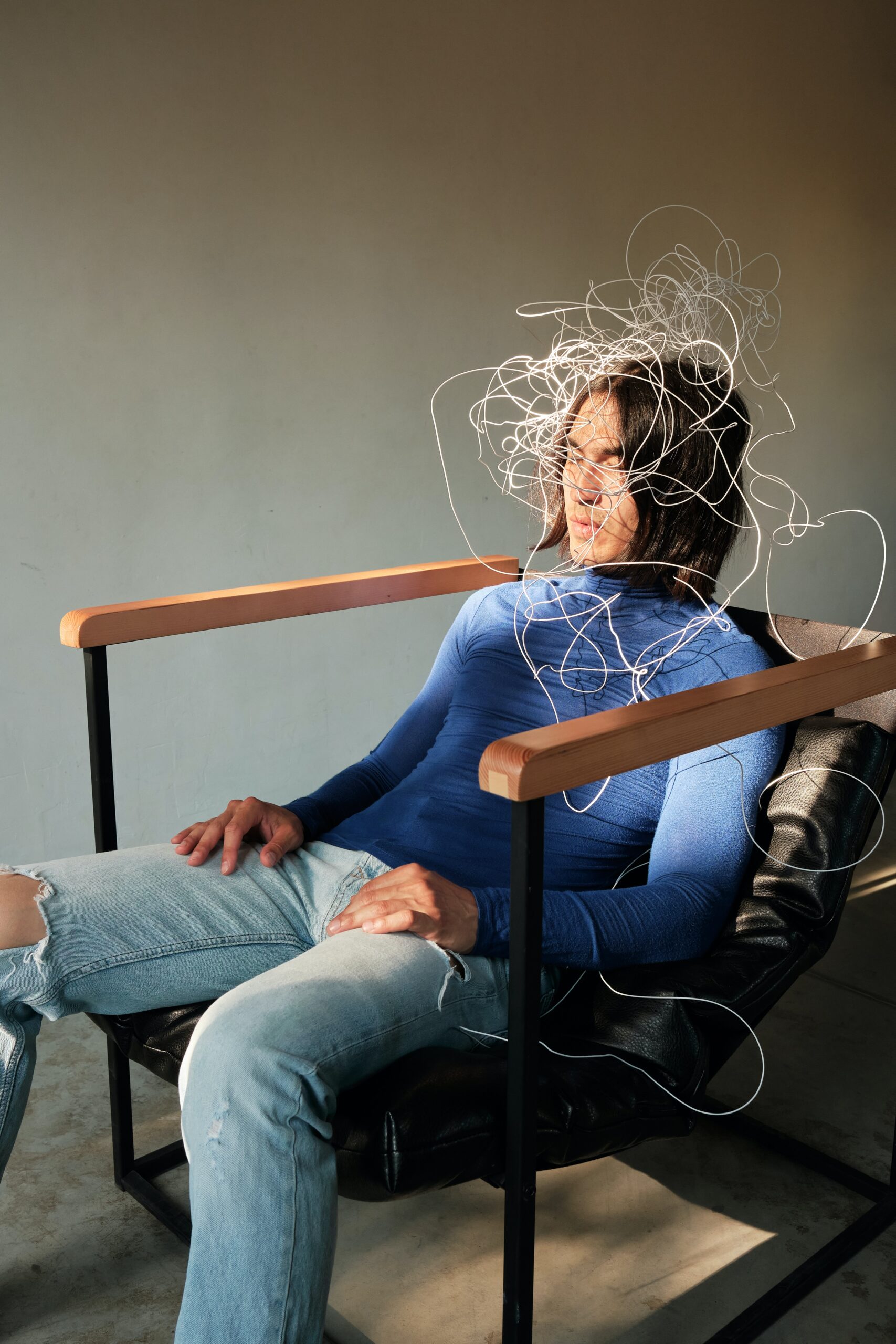 A person sitting in a chair, head surrounding by chaotic, white wires 