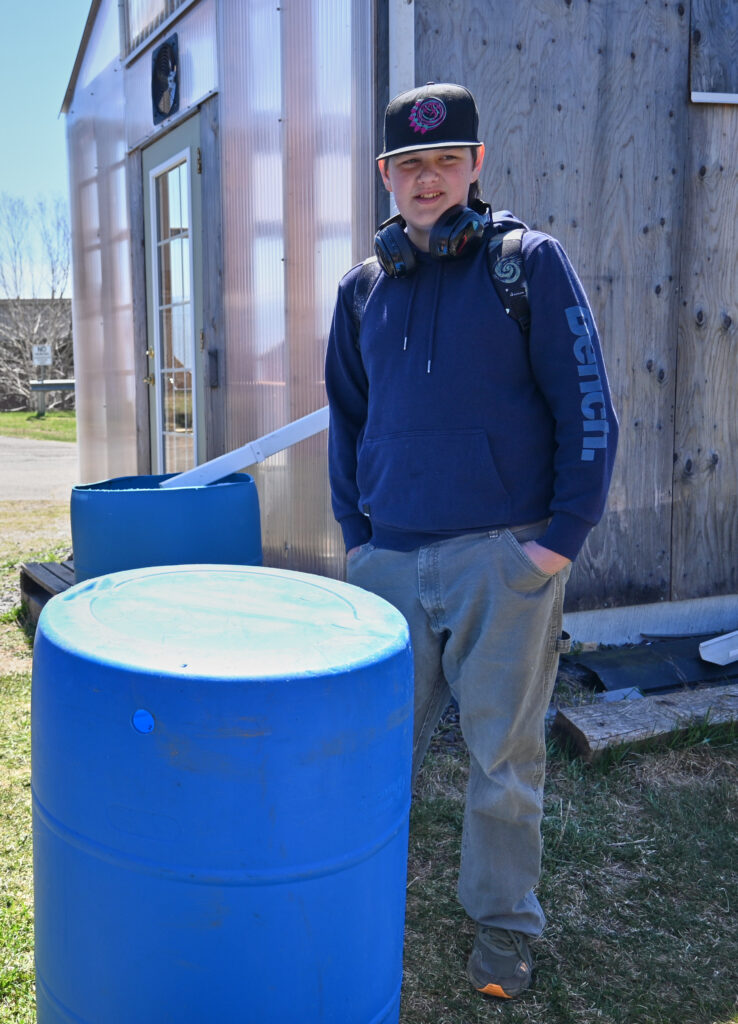 A student stands next to the rain barrels that the class installed next to the greenhouse 