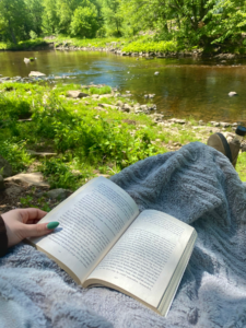 Photo d’un livre sur des genoux avec une rivière en arrière-plan 