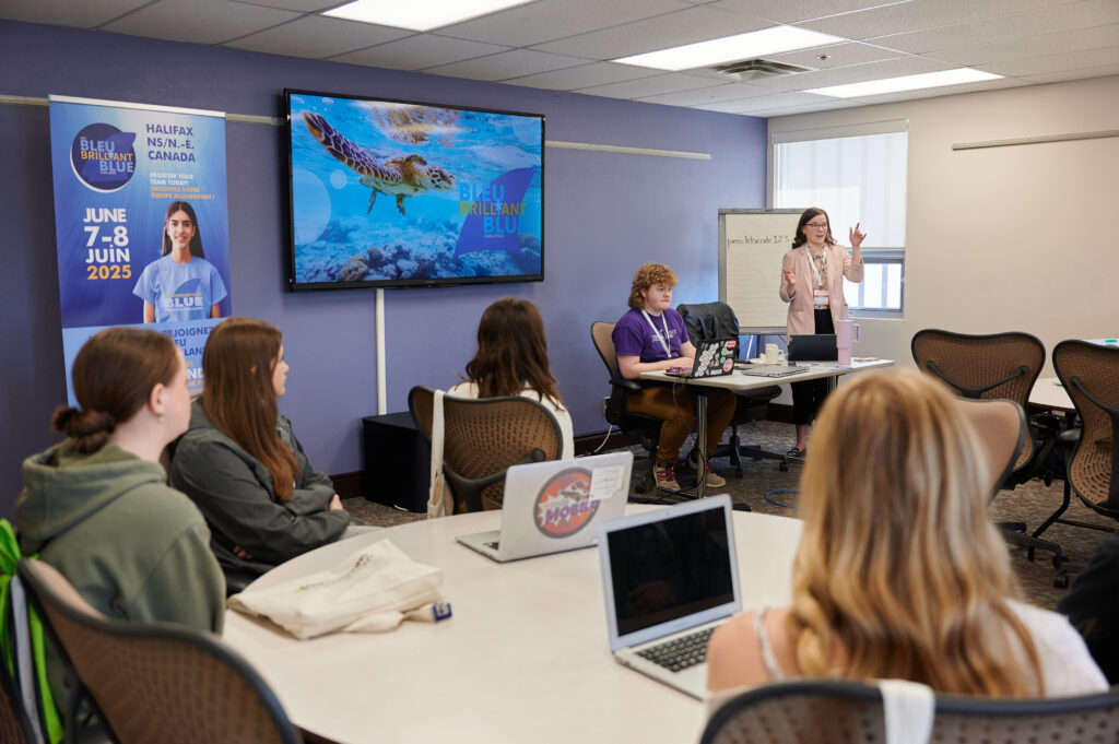 Students sitting at a table with laptops, watching a workshop presentation 