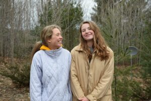 Two teenage girls stand in a forest, smiling