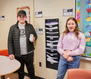 A photo of two students standing together, one is holding an energy meter